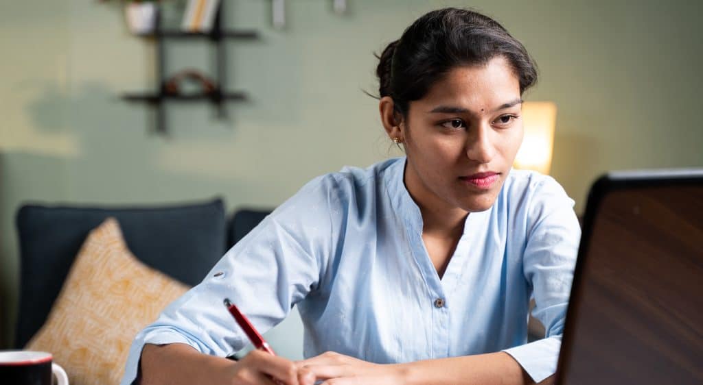 Woman looking at computer taking notes